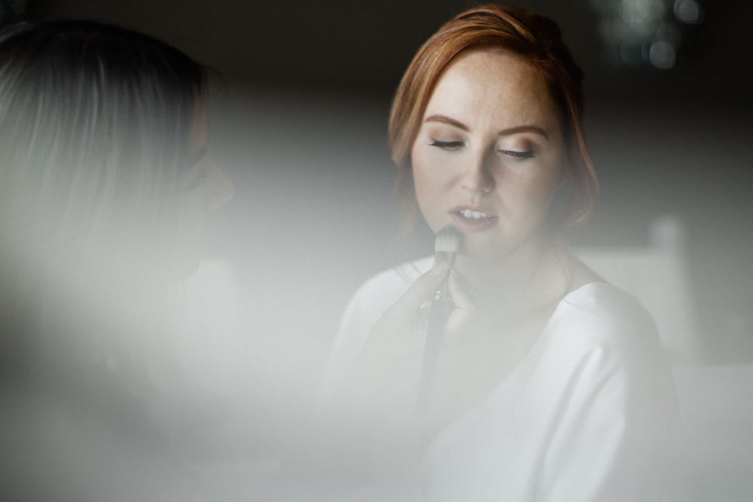 A makeup artist applies makeup to a bride, with a soft focus effect that enhances the intimate atmosphere.