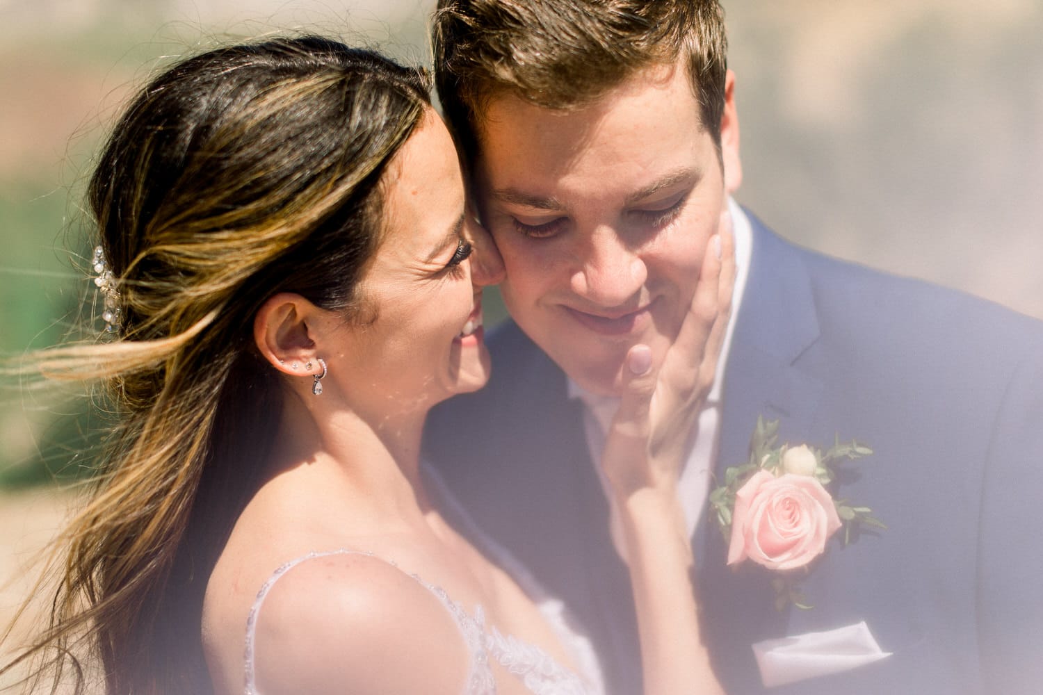 A joyful bride and groom share a loving gaze, surrounded by nature, with the bride gently touching the groom's face.