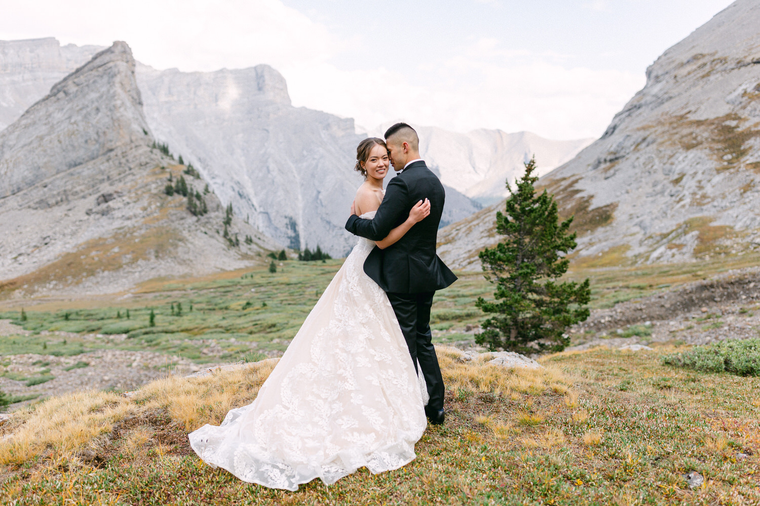 A newlywed couple embracing in a stunning mountain landscape, featuring rugged peaks and lush greenery.