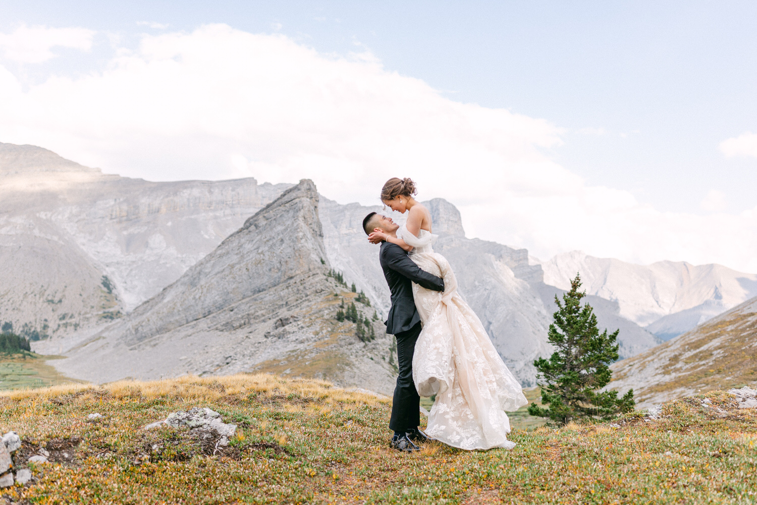 A groom lifting his bride in a picturesque mountain landscape, showcasing love and joy against a stunning natural backdrop.