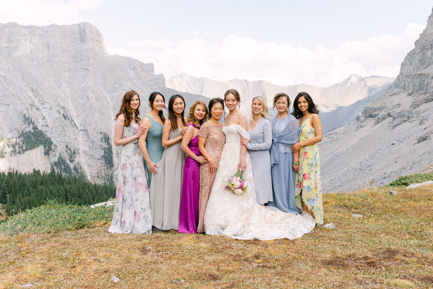 A joyful bridal party poses together in beautiful dresses against a stunning mountain backdrop, celebrating love and friendship.