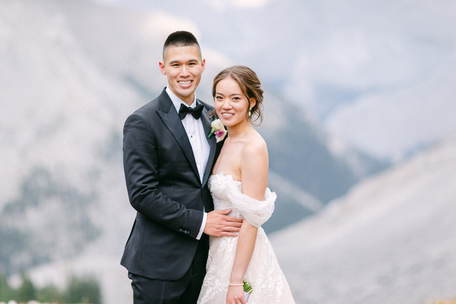 A happy couple in formal attire poses together with a mountain backdrop, showcasing their love and elegance.