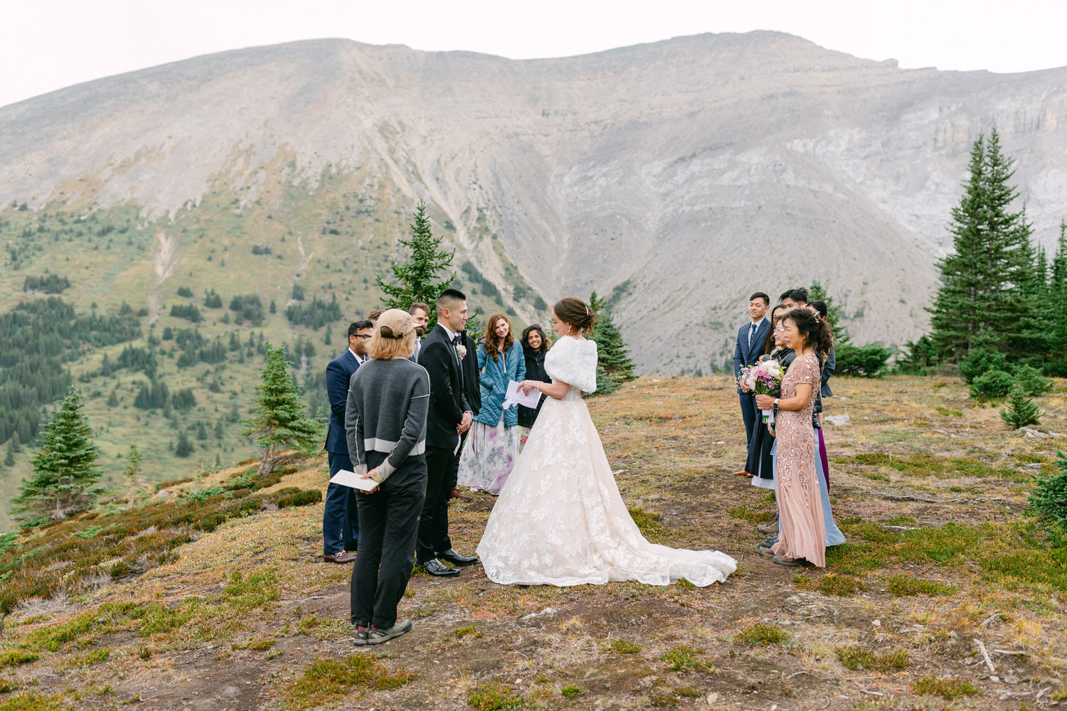 A couple exchanging vows in a scenic outdoor wedding ceremony surrounded by guests in a mountainous landscape.