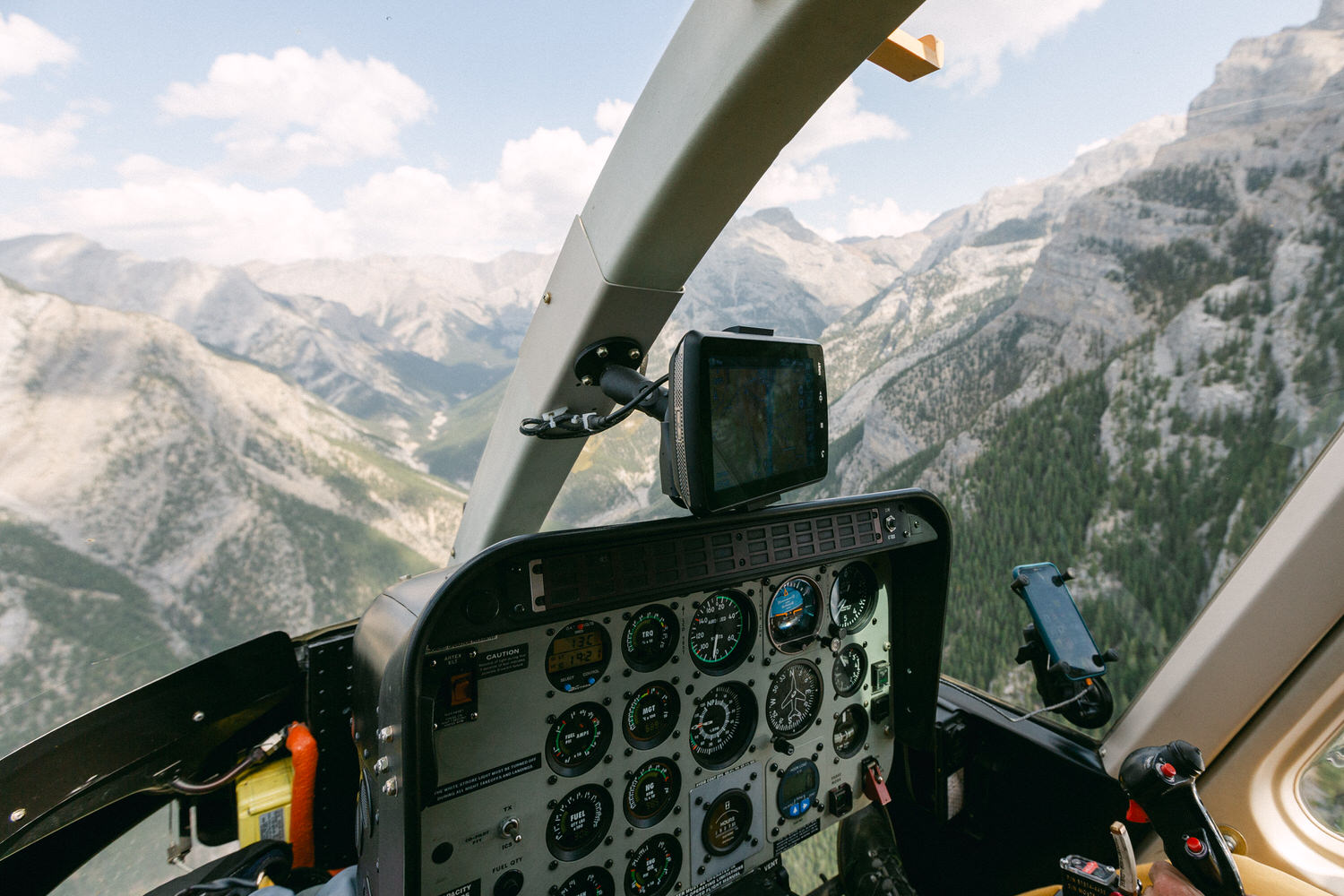 Aerial perspective from a helicopter cockpit showcasing flight instruments with mountain scenery in the background.