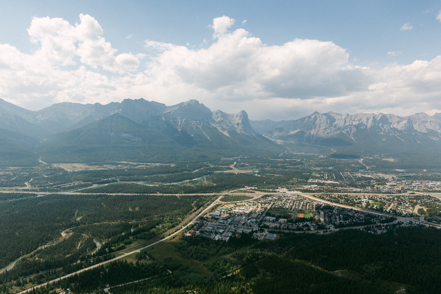 Aerial view of a lush green valley with a town nestled beneath majestic mountains and a cloudy sky.