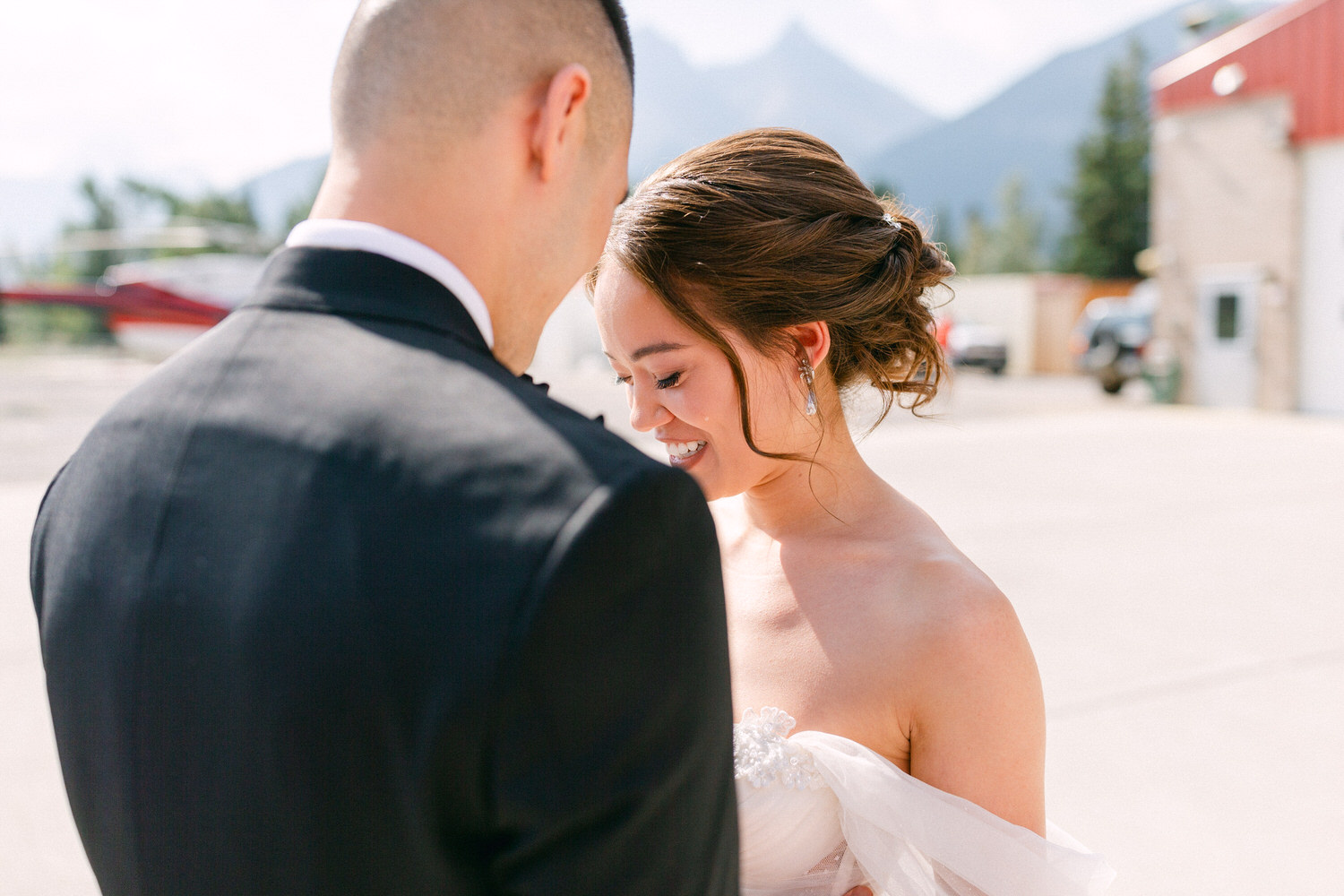 A bride smiles affectionately at her partner, capturing a heartfelt moment outdoors with mountains in the background.