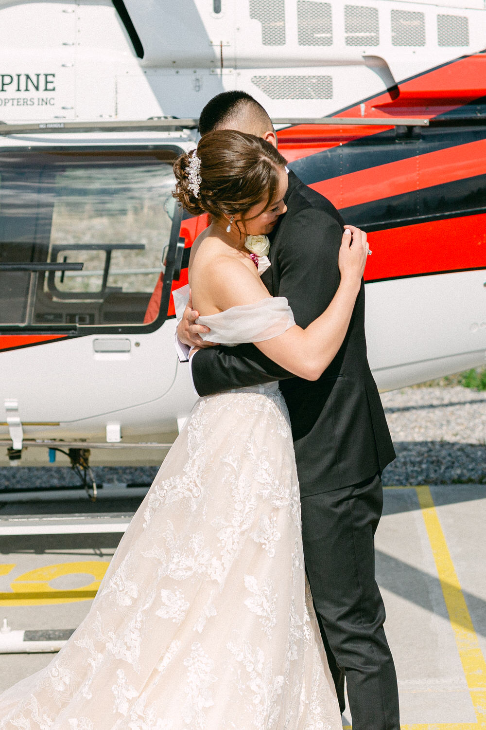 A couple shares a tender embrace on their wedding day, set against the backdrop of a helicopter, capturing a moment of joy and intimacy.