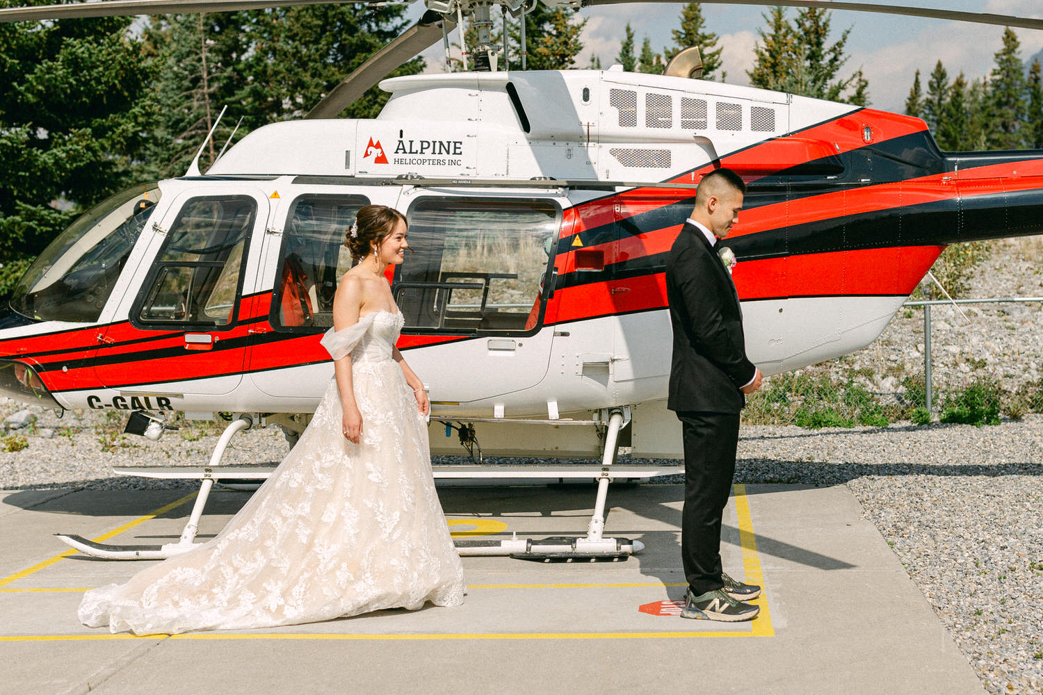 Bride and groom standing back-to-back near a helicopter, preparing for their wedding reveal.