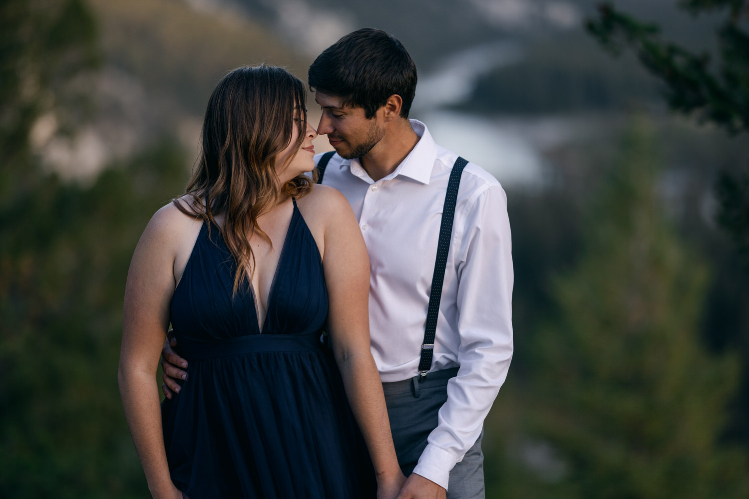 A couple shares an intimate moment outdoors, gazing into each other's eyes amidst a beautiful natural backdrop.