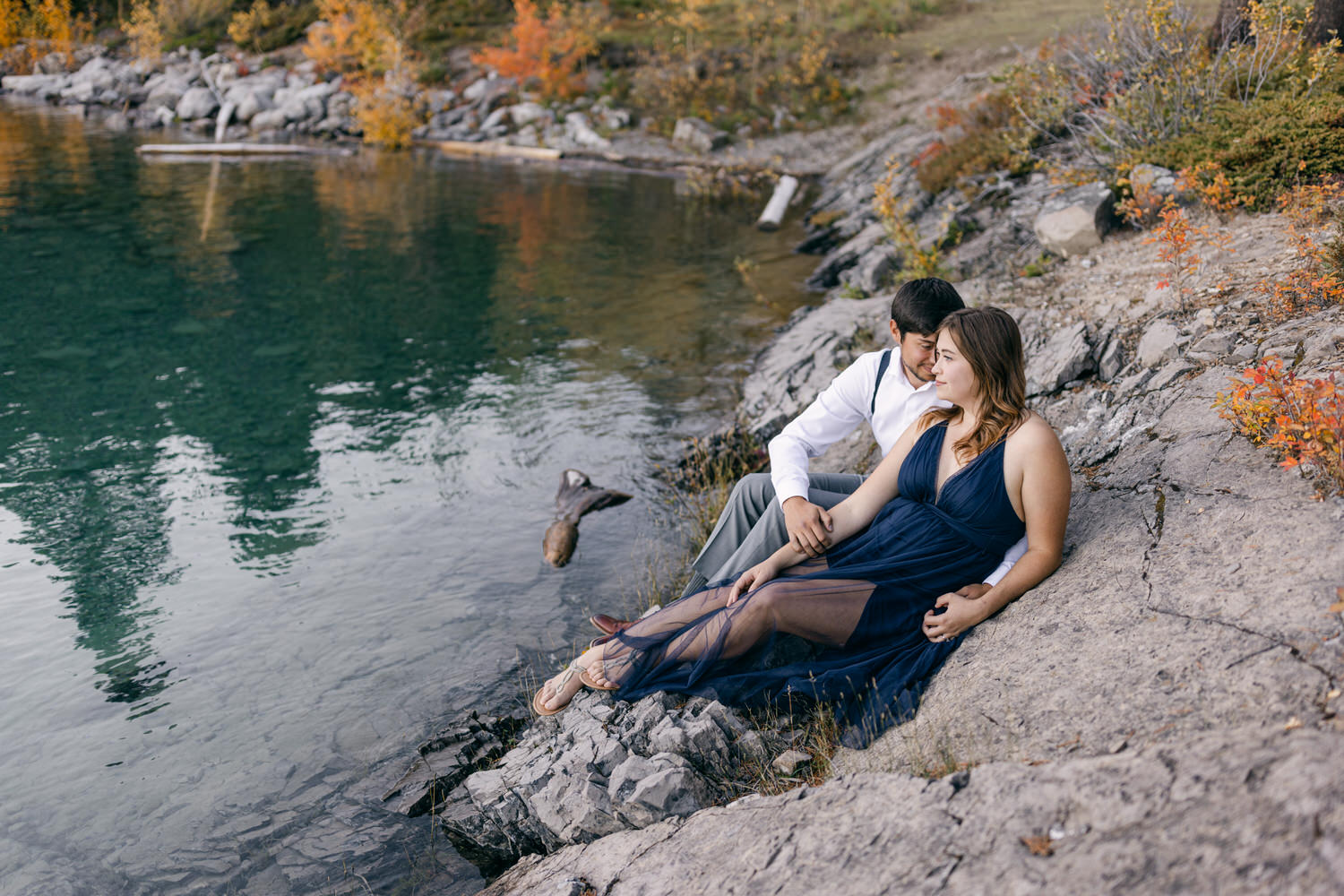 A couple enjoys a serene moment by a tranquil lake surrounded by autumn foliage.