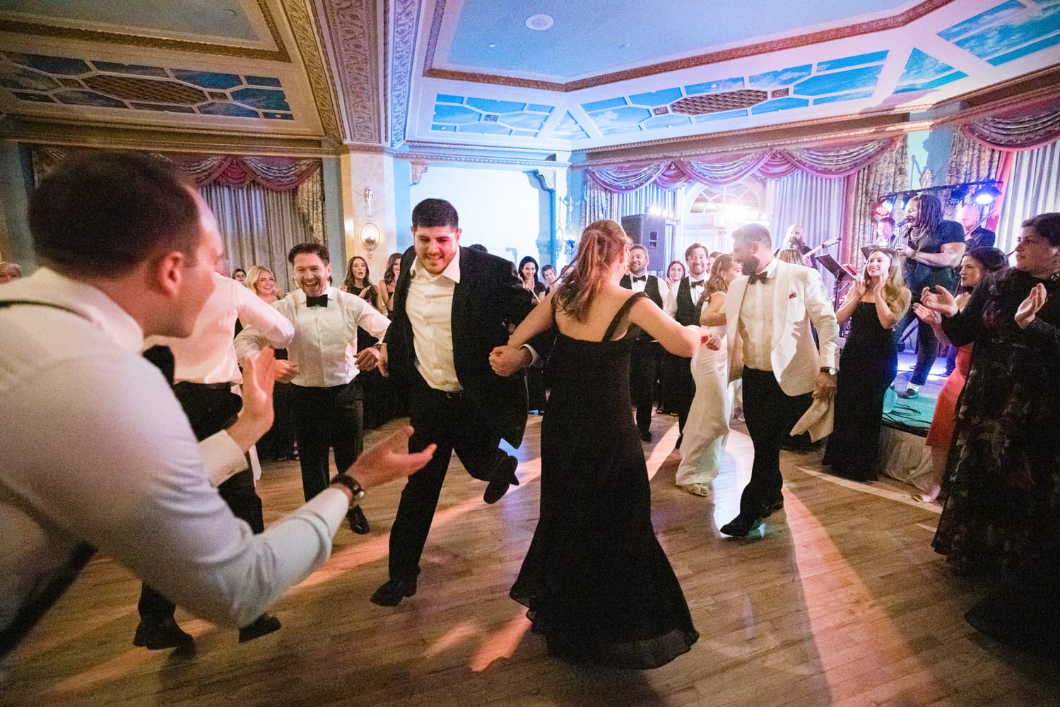 Guests joyfully dancing together at a wedding reception in an elegant venue, surrounded by friends and live music.