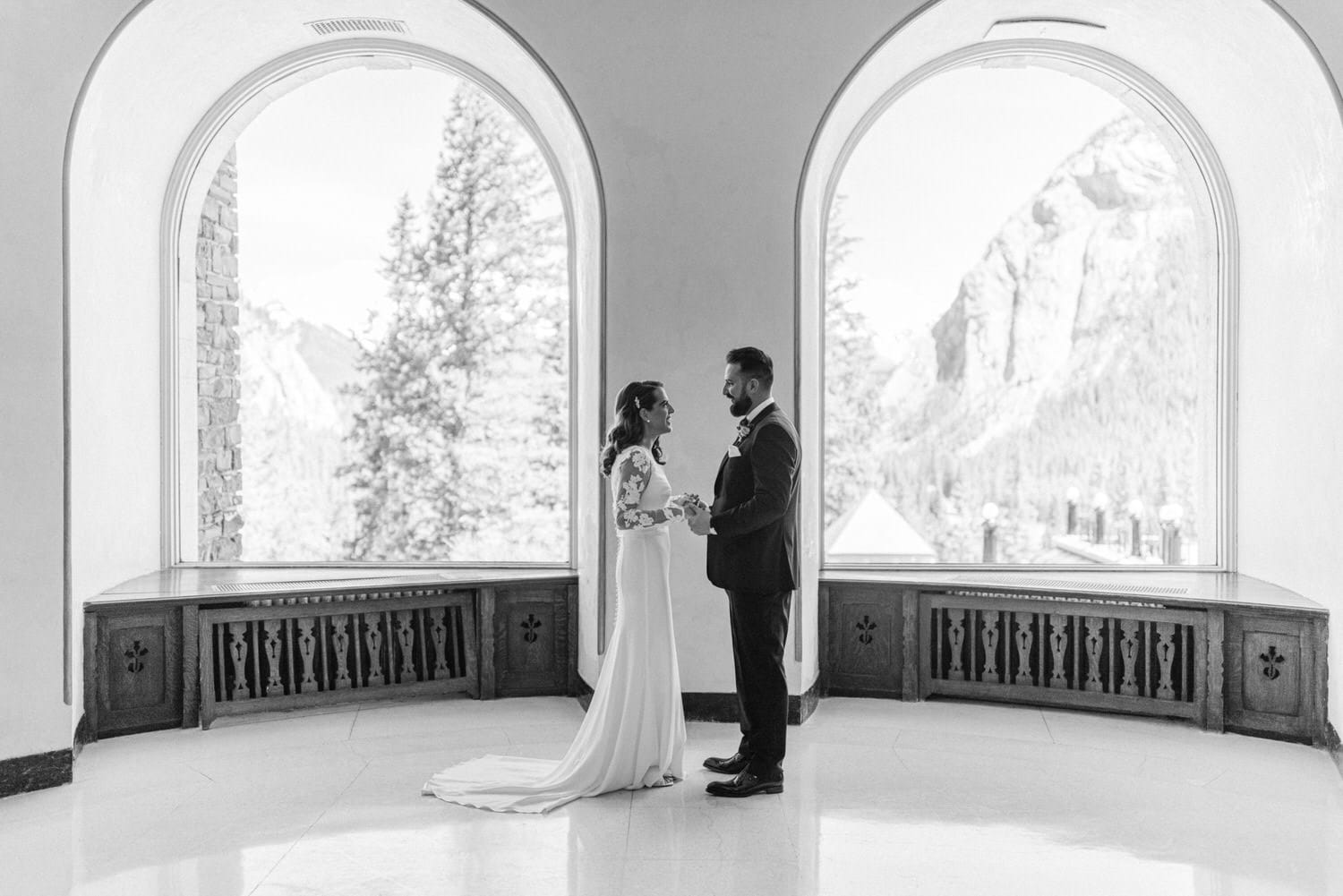 A bride and groom share a heartfelt moment in a beautifully arched room, framed by stunning mountain views.