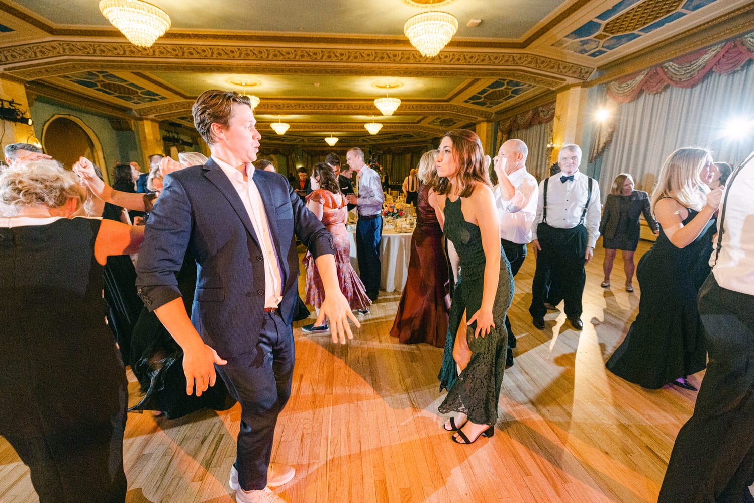 A lively dance floor scene featuring elegantly dressed guests enjoying a festive atmosphere with colorful lighting and vibrant energy.