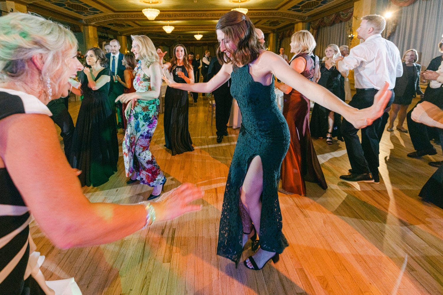 A lively dance floor filled with elegantly dressed guests enjoying a celebration, featuring a woman in a green dress dancing in the foreground.