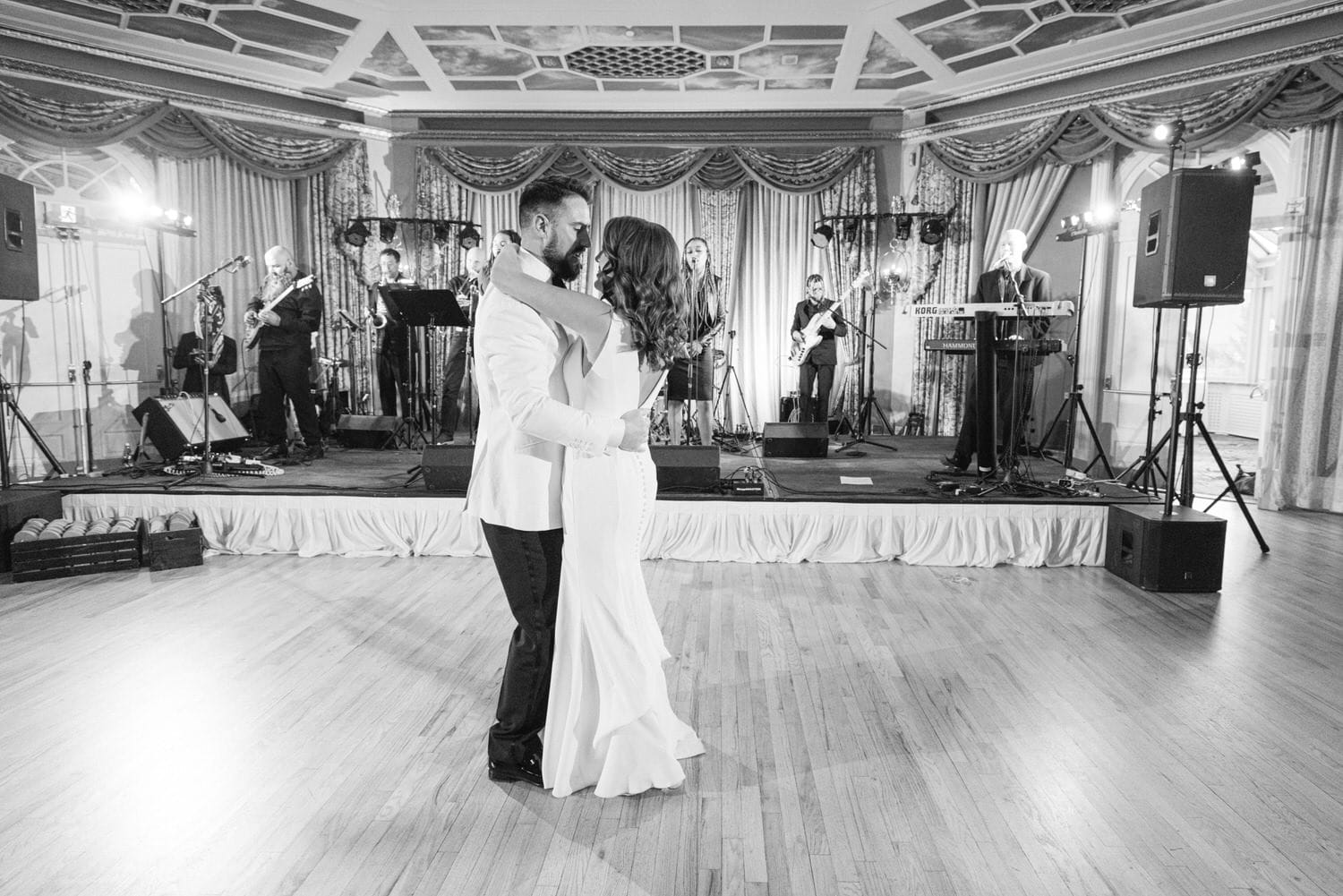 A couple shares a romantic dance on the floor, surrounded by a live band performing in the background, set in a beautifully decorated venue.