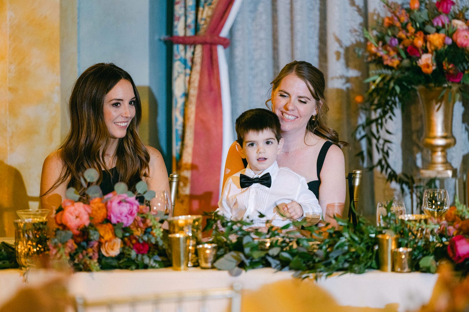 A joyful moment featuring two women and a young boy at a beautifully decorated table with vibrant floral arrangements.