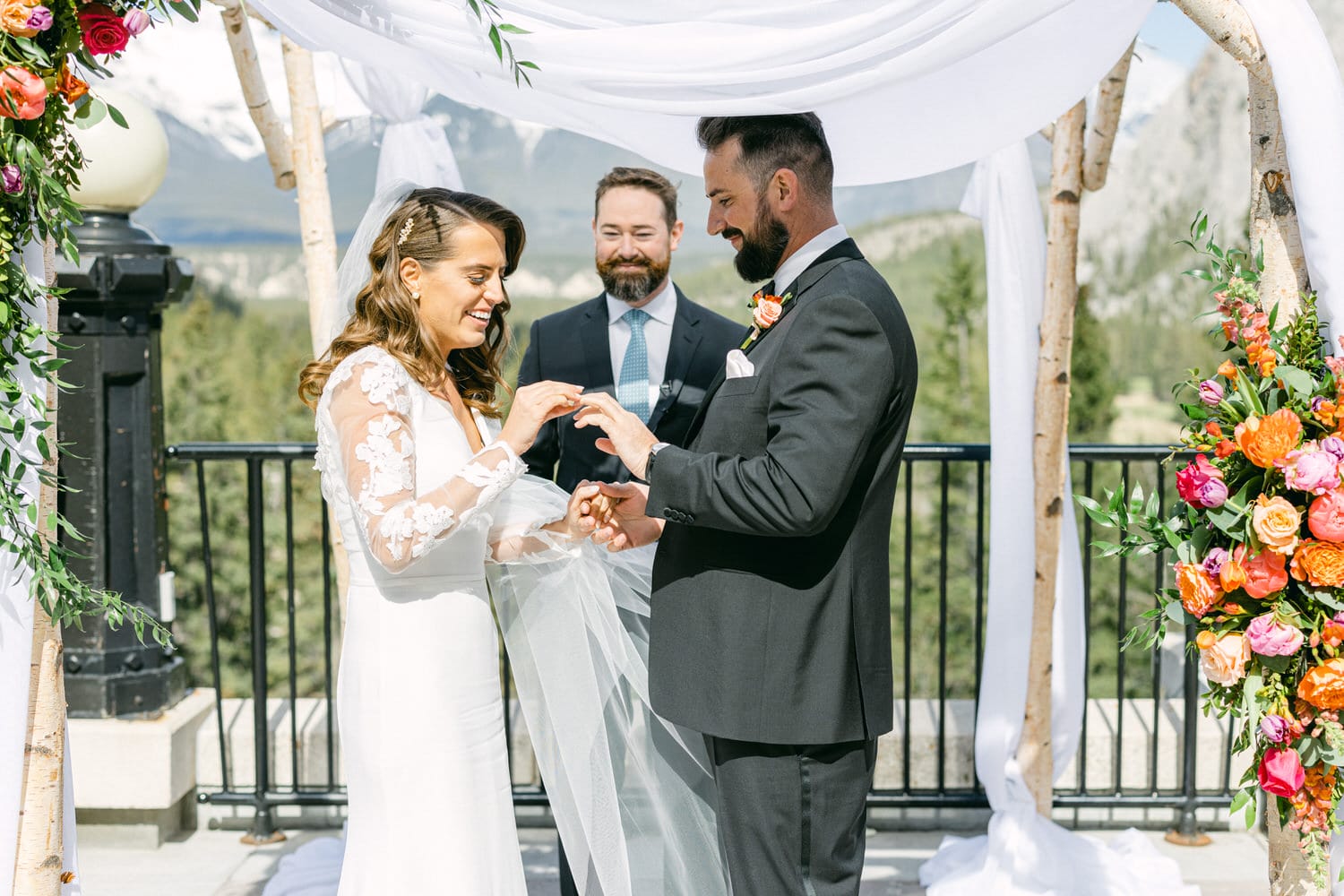 A couple exchanges rings during their wedding ceremony, surrounded by floral decorations and a beautiful mountain backdrop.