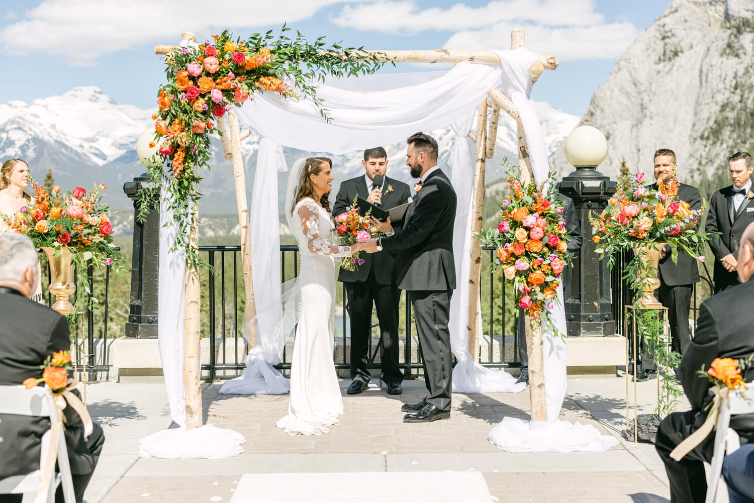 A couple exchanges vows under a floral arch at a picturesque mountain wedding ceremony.