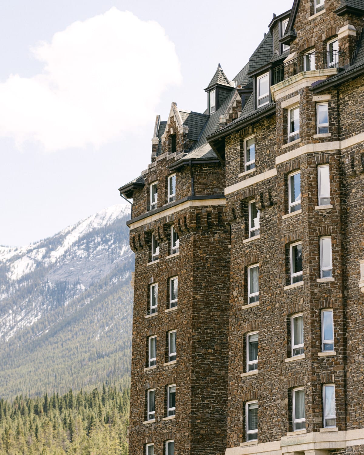 A close-up view of a historic stone Banff Springs Hotel featuring detailed architecture, with snow-capped mountains in the background under a clear sky.