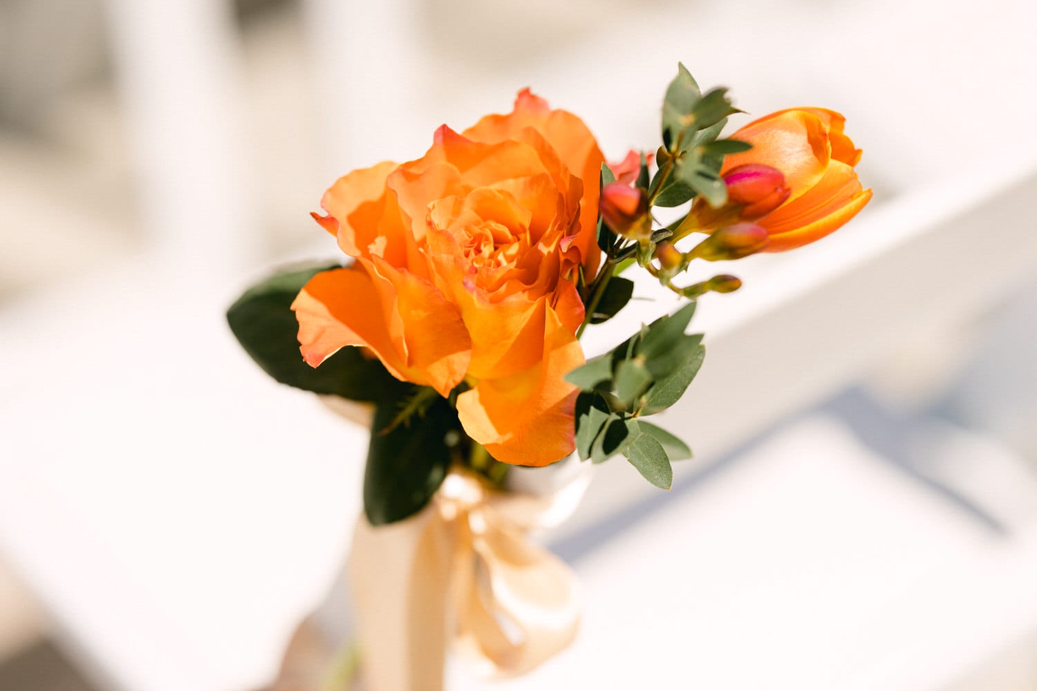 A close-up of a vibrant orange rose with green leaves and buds, elegantly tied with a ribbon, set against a softly blurred background.