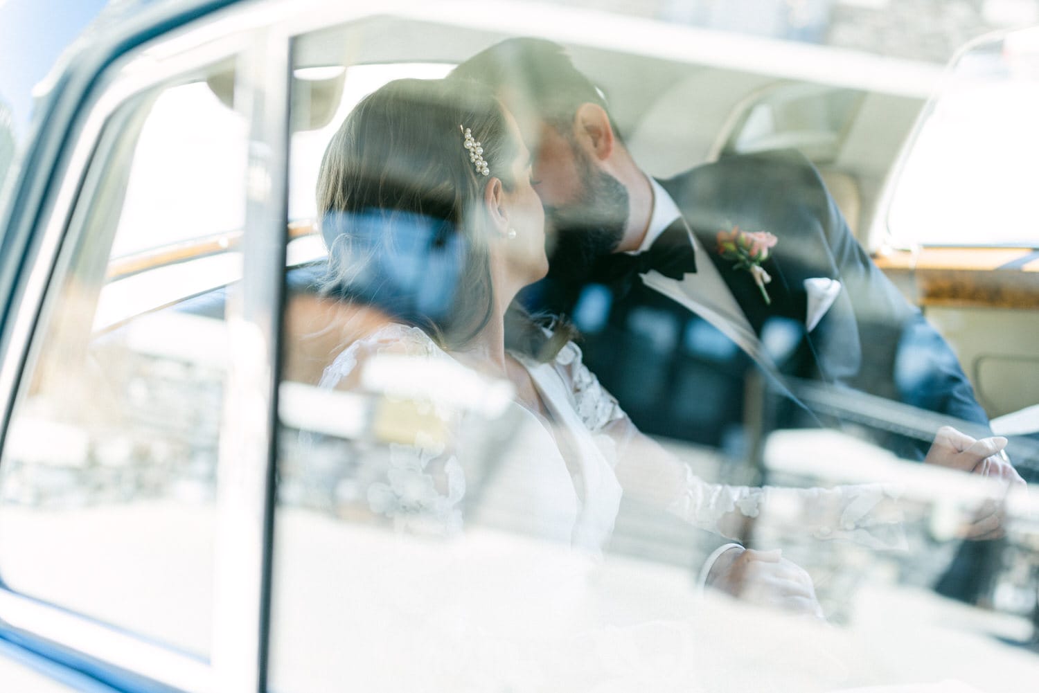 A couple sharing a kiss inside a vintage car, framed by the car's window reflections, capturing a tender and romantic moment.