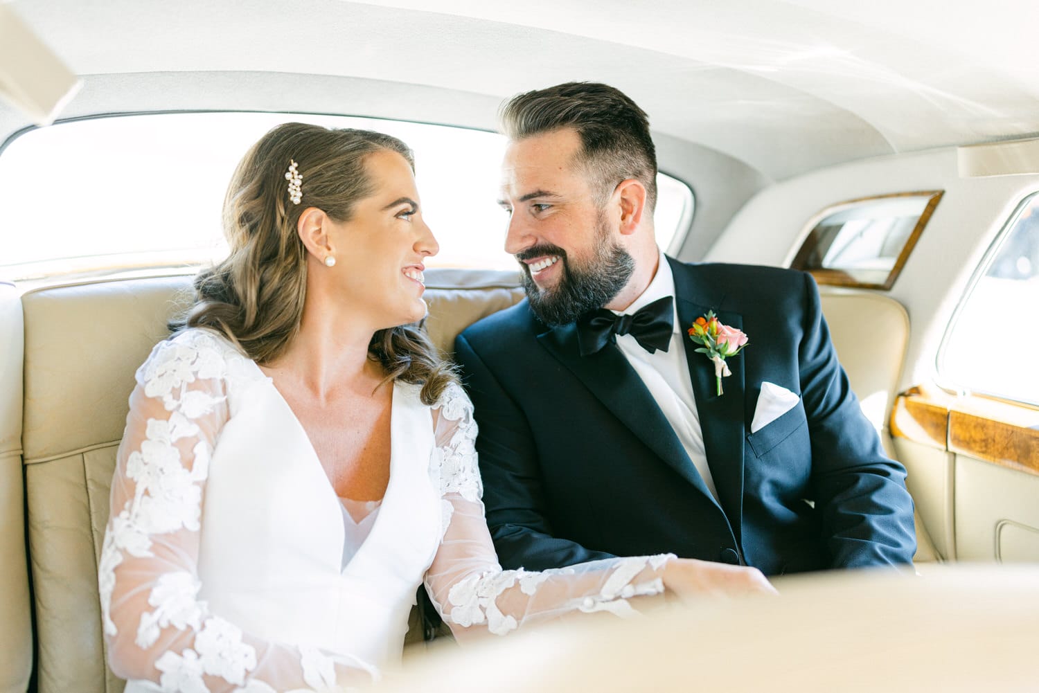 A bride and groom share a loving glance while seated in the back of a classic car, radiating happiness and elegance on their special day.