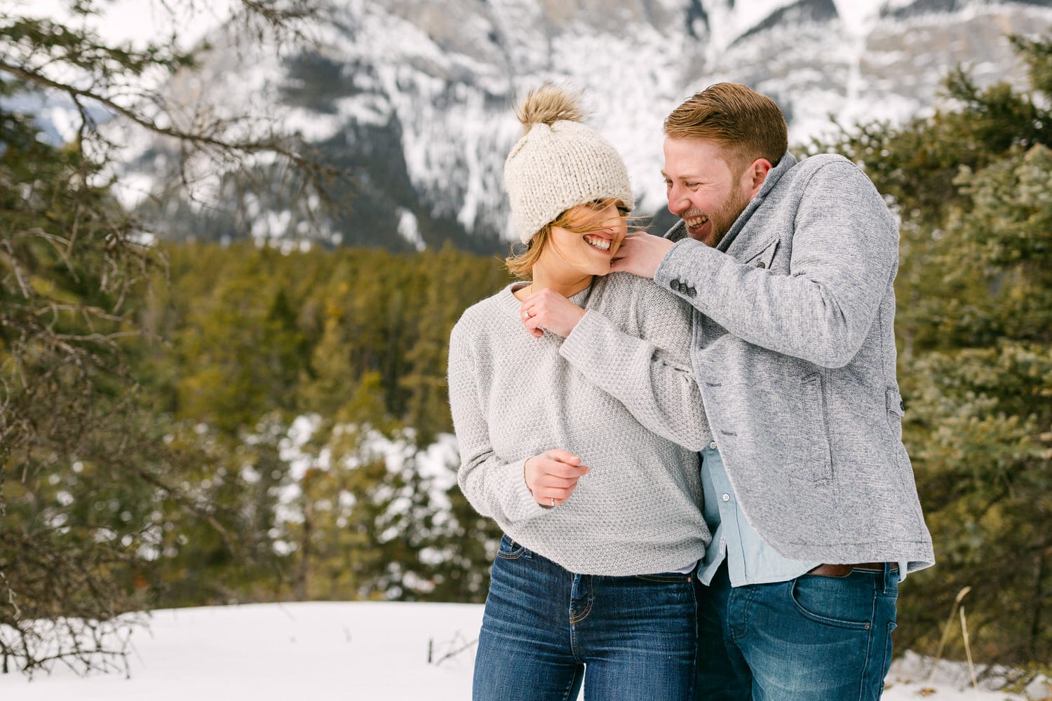 A couple playfully enjoying the snowy outdoors, laughing together with a scenic mountain backdrop.