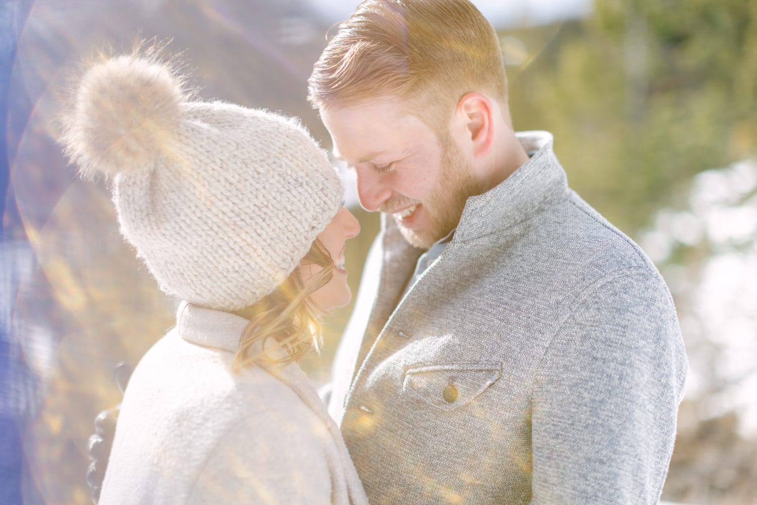 A couple sharing a joyful moment outdoors in winter attire, surrounded by sparkling sunlight.