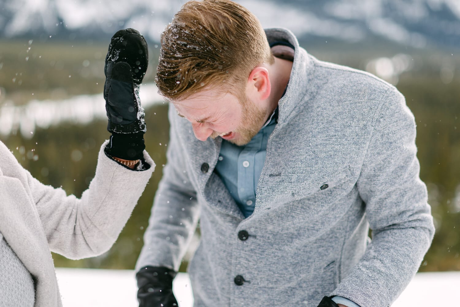 A man reacts playfully as snow is tossed at him during a snowy outdoor adventure in a mountainous landscape.