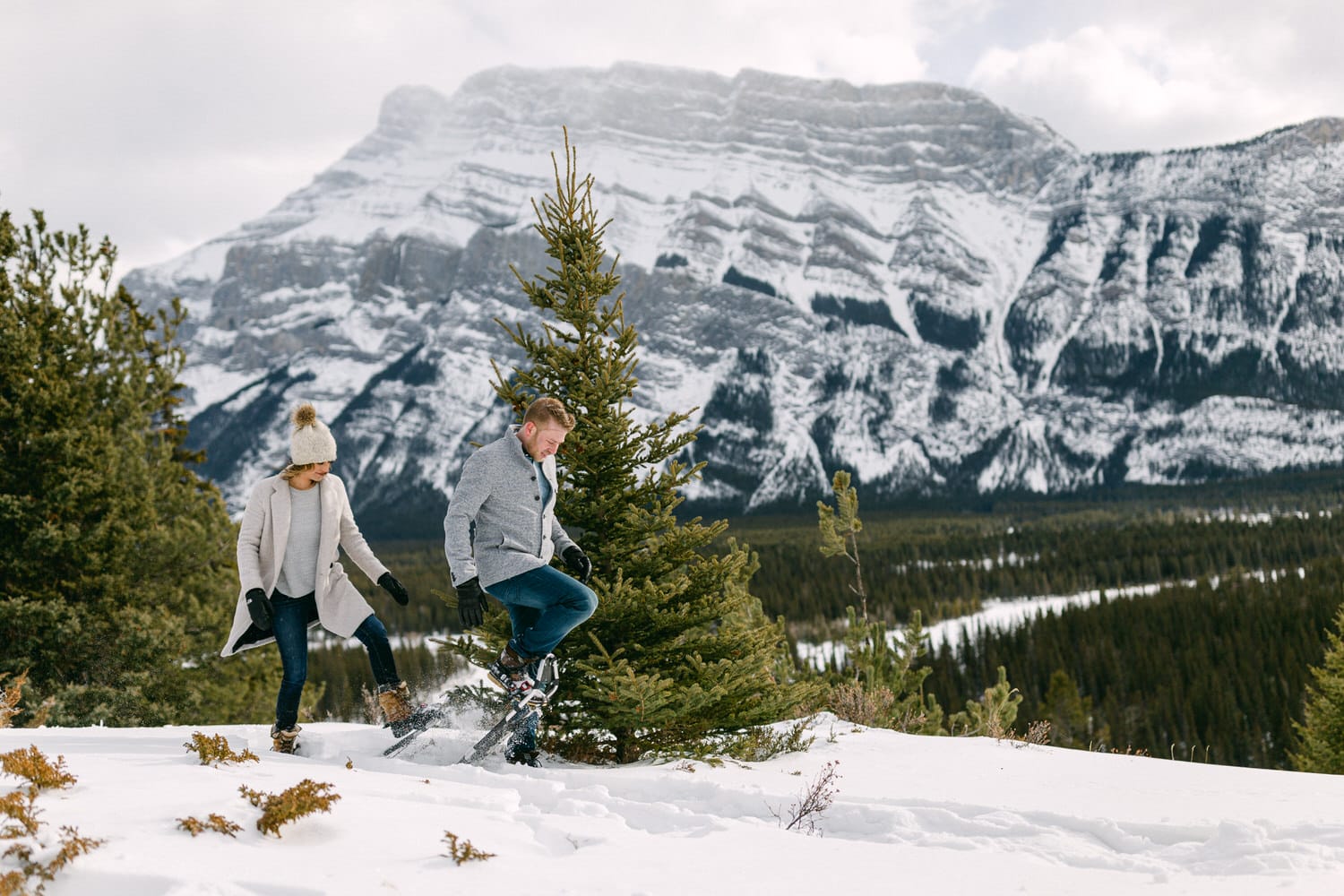 Couple snowshoeing through a snowy landscape with mountains in the background.