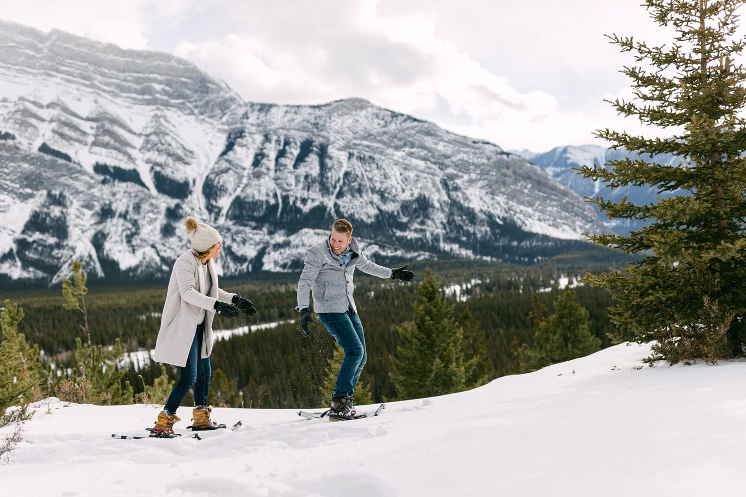 Couple enjoying snowshoeing in a picturesque snowy landscape with mountains in the background.