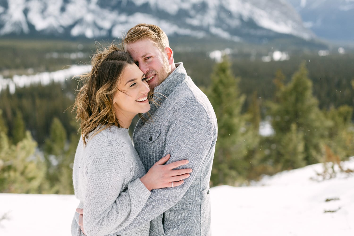 A joyful couple enjoys a loving embrace against a snowy mountain backdrop, capturing a moment of happiness and connection.