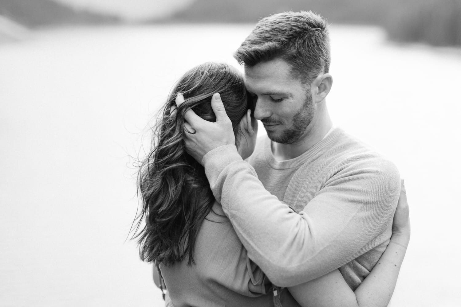 A couple sharing a tender moment, wrapped in each other's arms, with a serene lake in the background.