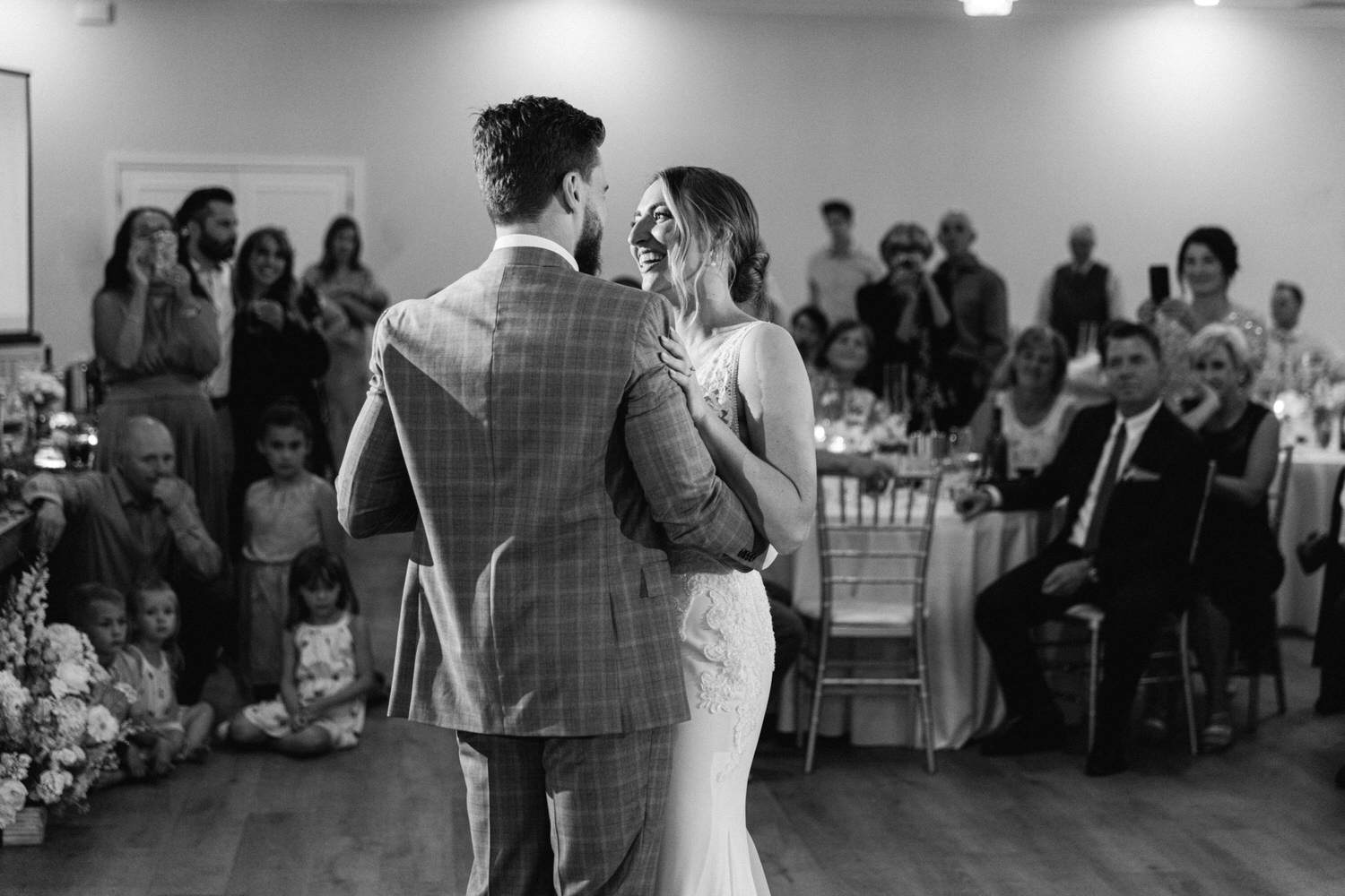 A couple shares a joyful moment during their first dance at a wedding reception, with guests observing and enjoying the occasion.