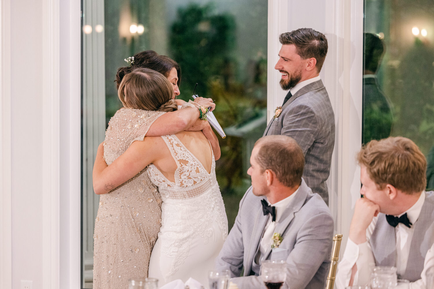 A touching moment of two women embracing during a wedding reception, surrounded by smiling guests at a beautifully decorated table.