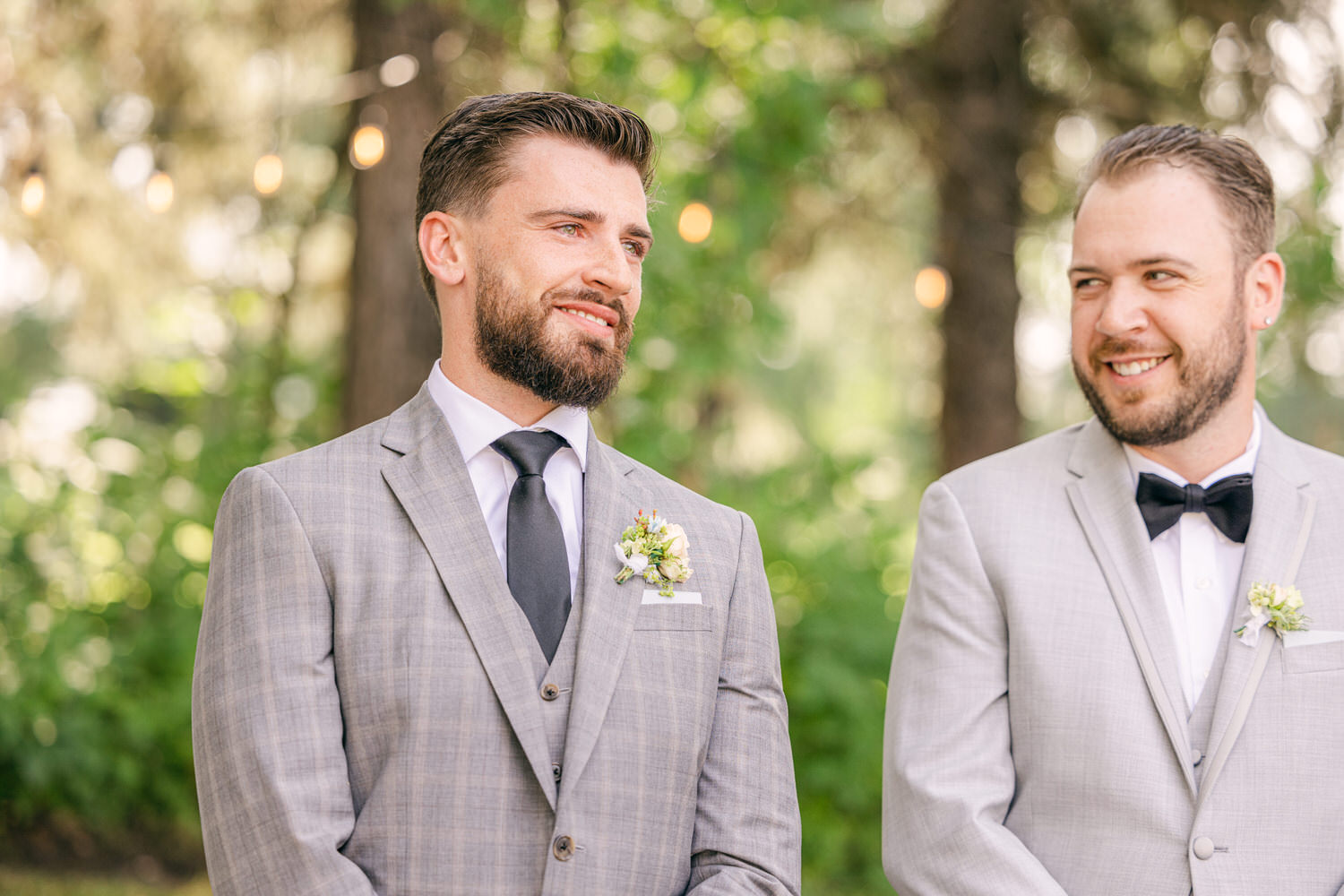 Two well-dressed men enjoy a joyful moment outdoors, with soft lighting and greenery in the background.