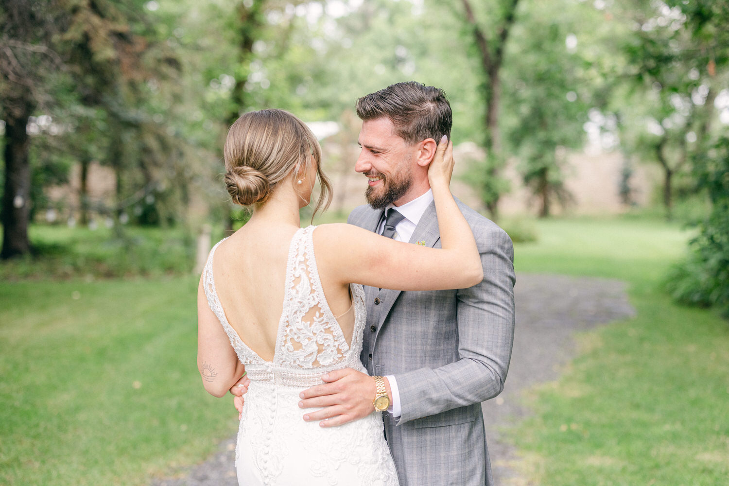 A joyful couple shares a loving moment outdoors, showcasing their elegant wedding attire and intimate connection amidst a lush green background.