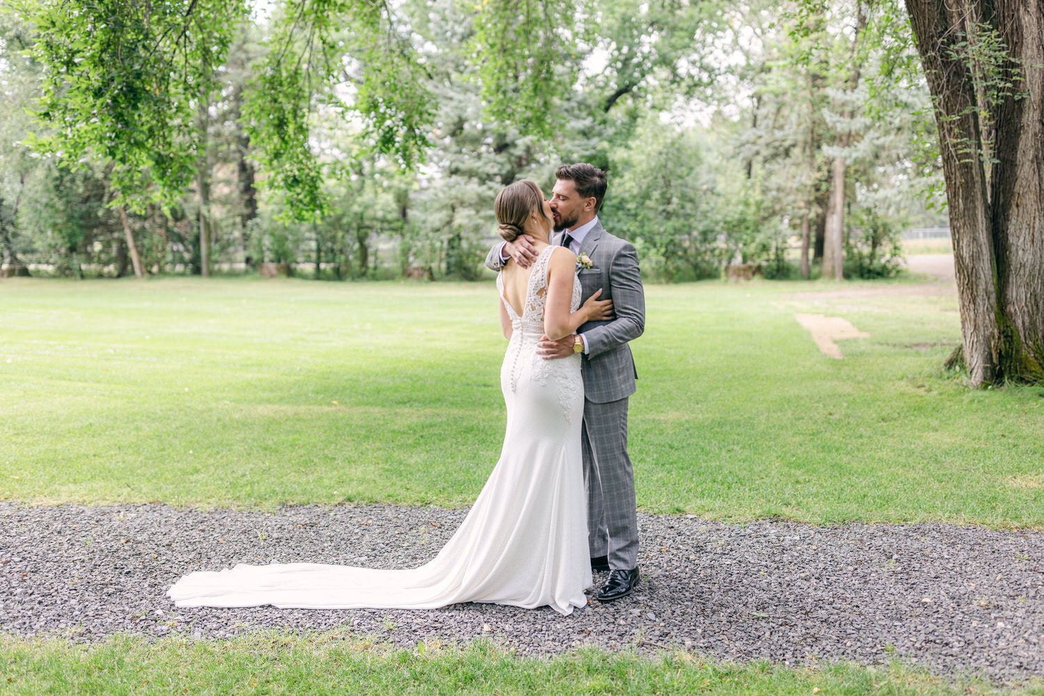 A couple sharing a tender moment outdoors, surrounded by greenery, the bride in a white gown and the groom in a gray suit.