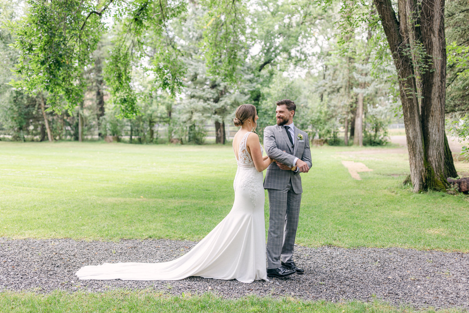 Wedding Couple in Nature::A joyful couple in wedding attire stands on a gravel path surrounded by lush greenery, sharing a moment together.