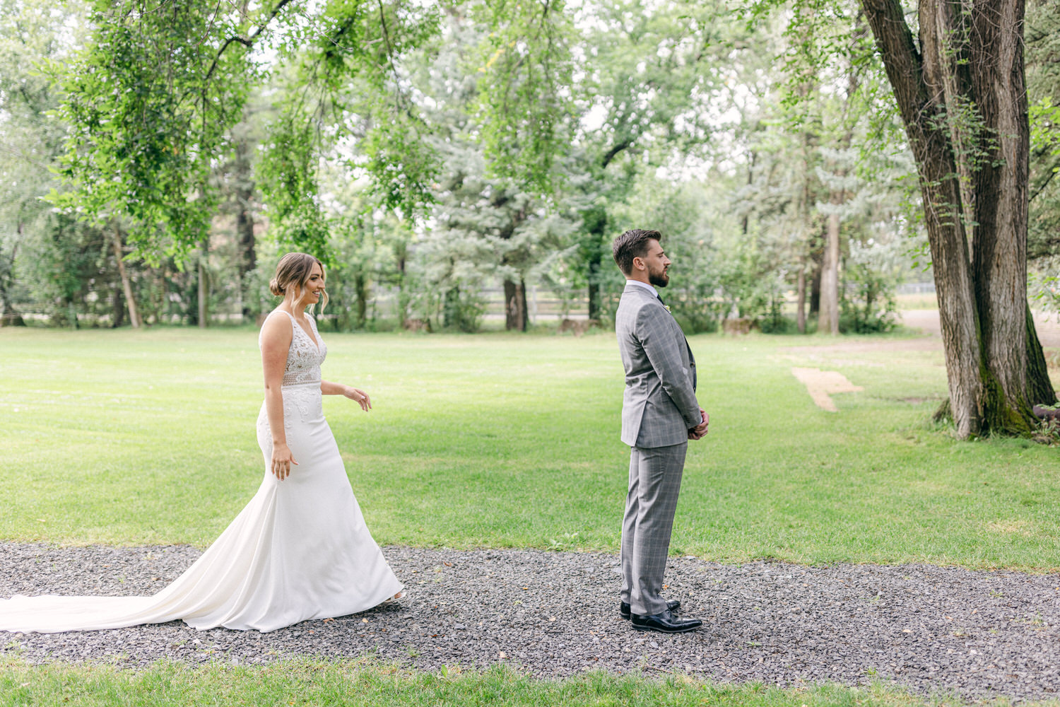 A bride approaches her groom for their first look, surrounded by lush greenery in a serene outdoor setting.