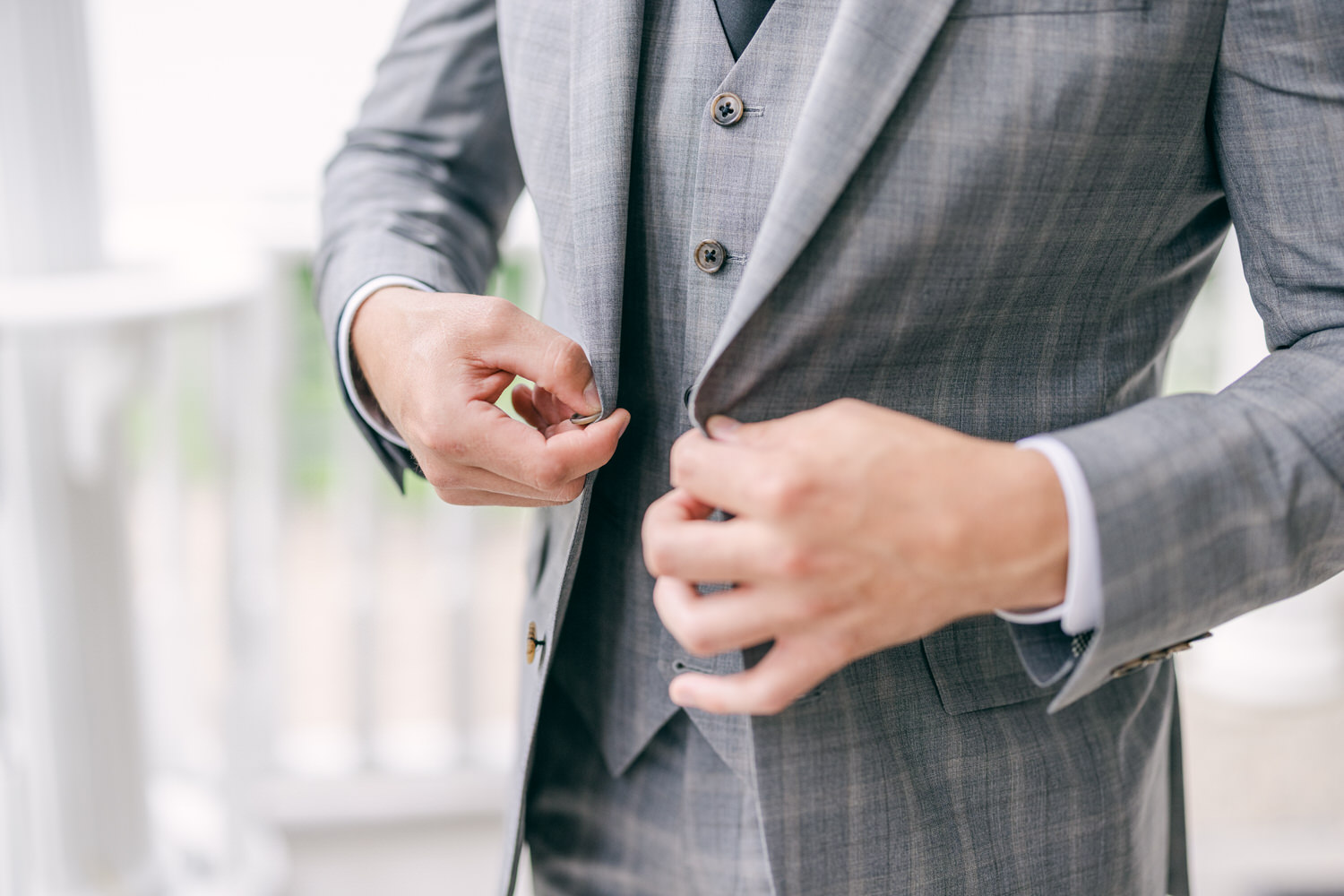 A close-up of a man adjusting the buttons of a well-fitted gray suit jacket.