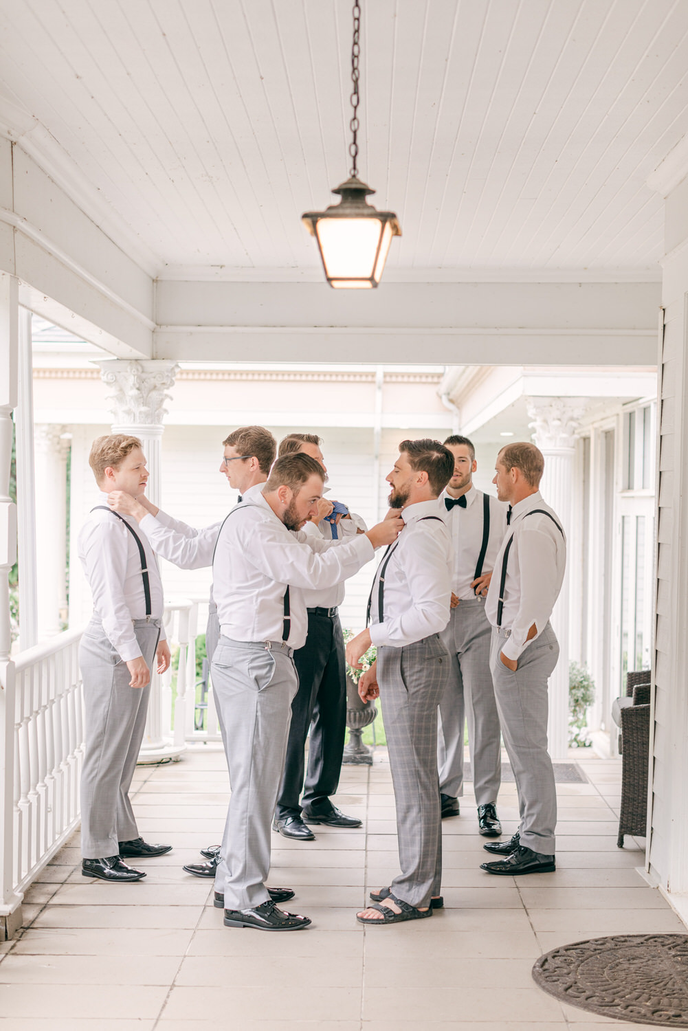 A group of well-dressed groomsmen adjusting ties and shirts on a porch, showcasing camaraderie and excitement before the ceremony.