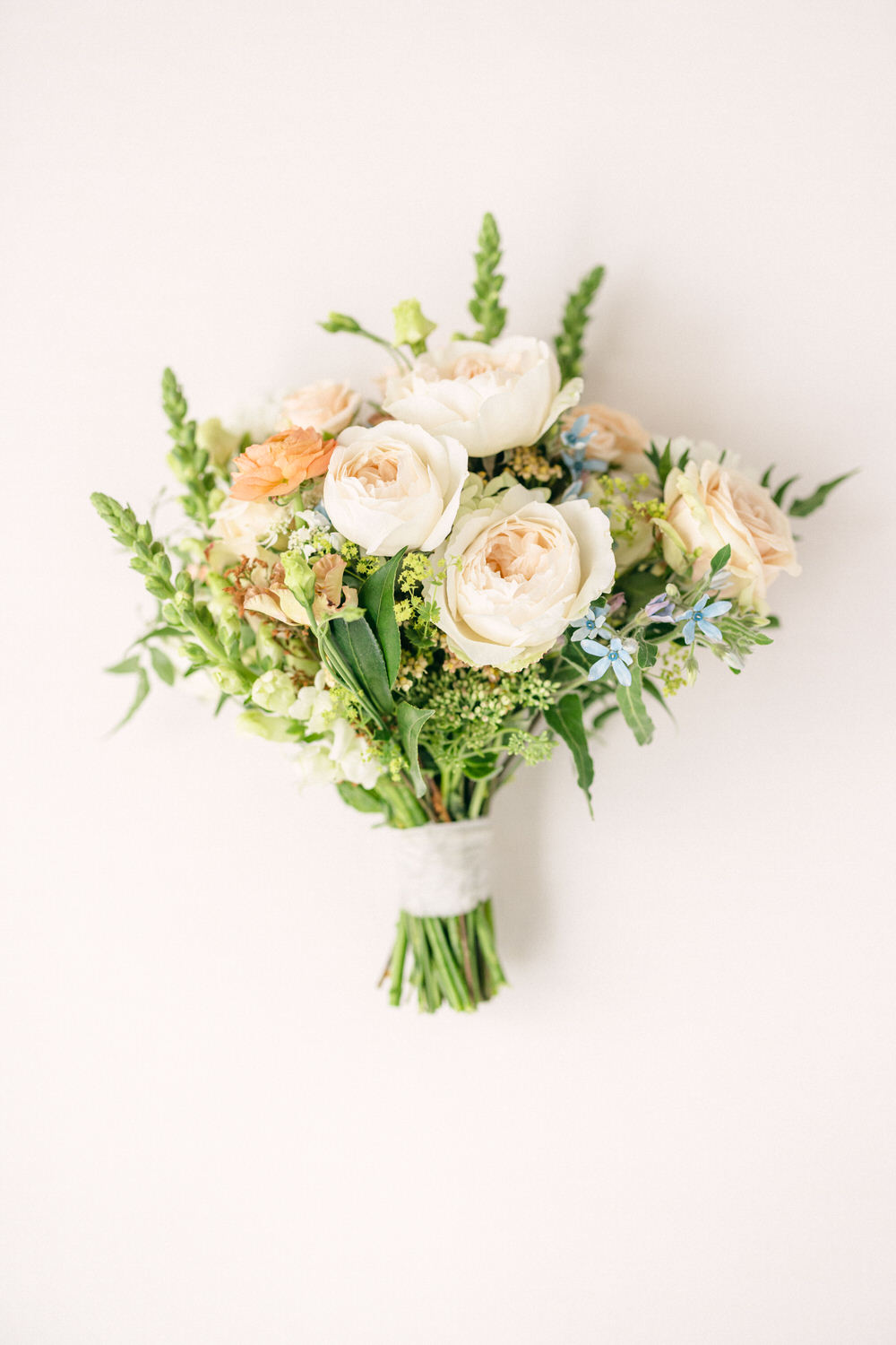 A beautifully arranged bouquet featuring soft peach and white roses, complemented by greenery and small blue flowers against a light background.