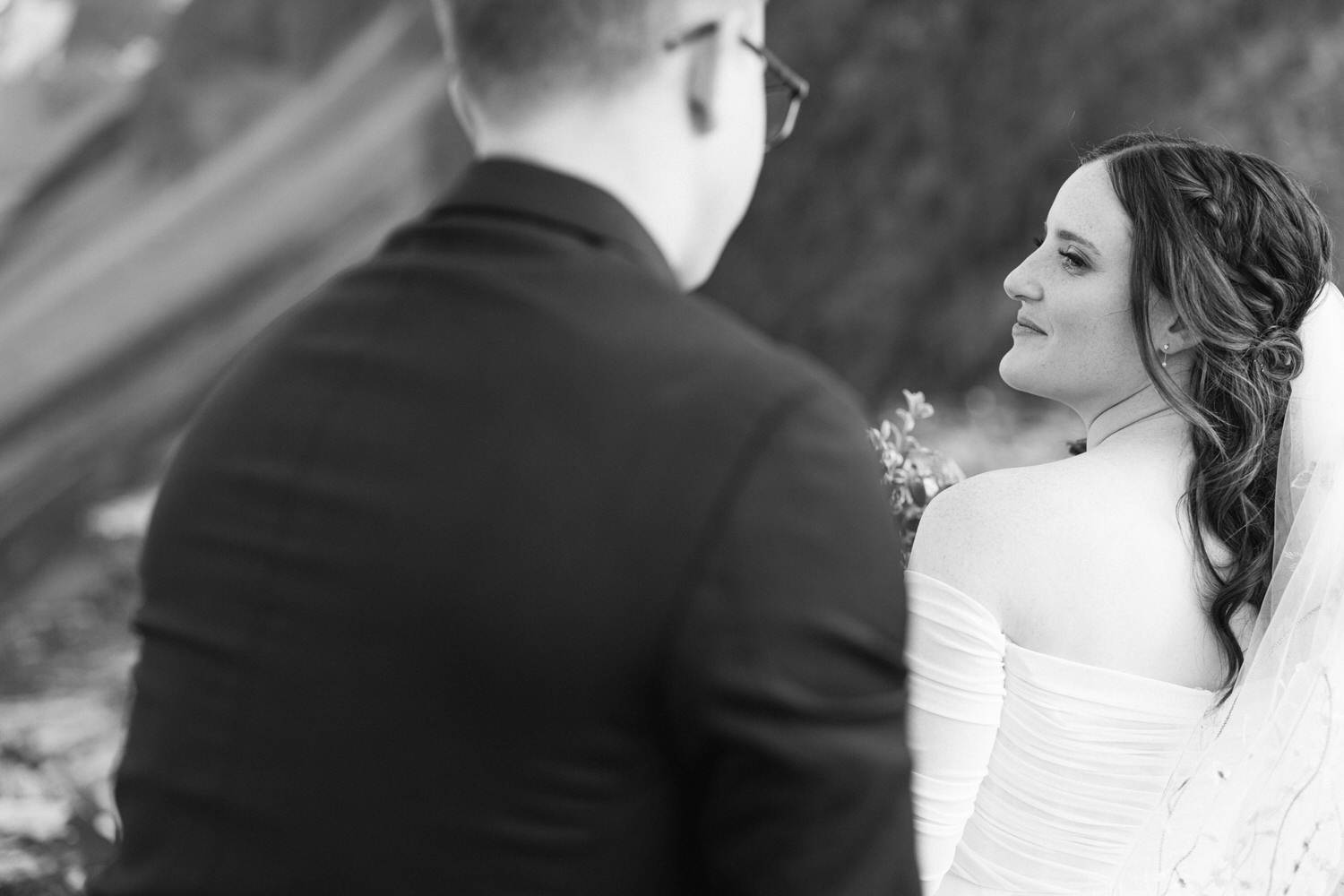 Bride looking back at her partner during an intimate outdoor ceremony, dressed in a white gown with a veil.