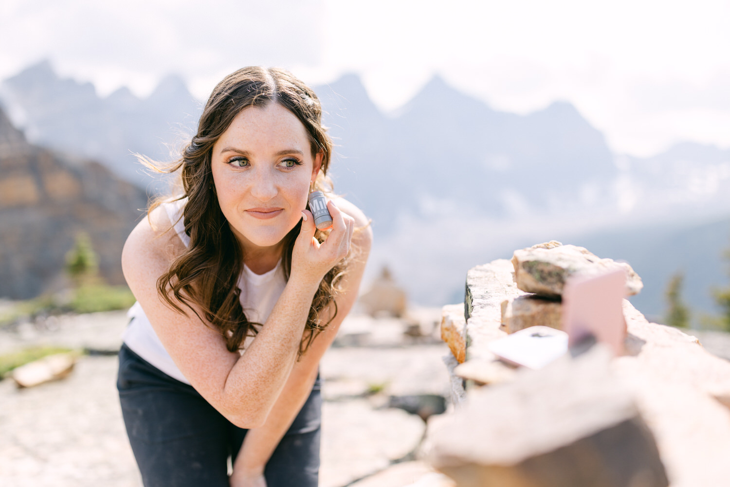 A woman applying essential oil to her neck in a scenic mountain landscape, showcasing a serene and natural beauty routine.