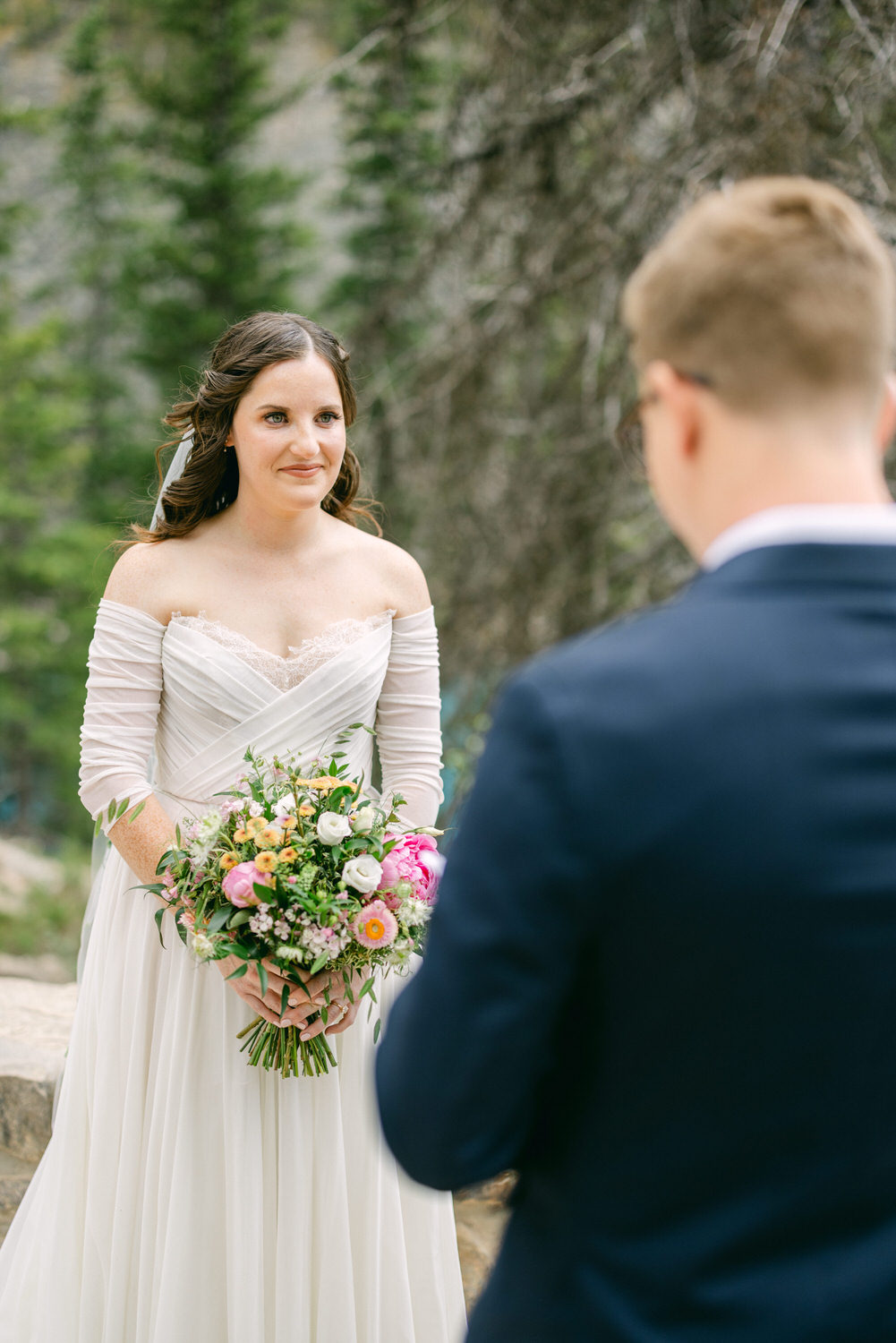 A bride holding a colorful bouquet stands before a groom, surrounded by lush greenery during an emotional outdoor ceremony.