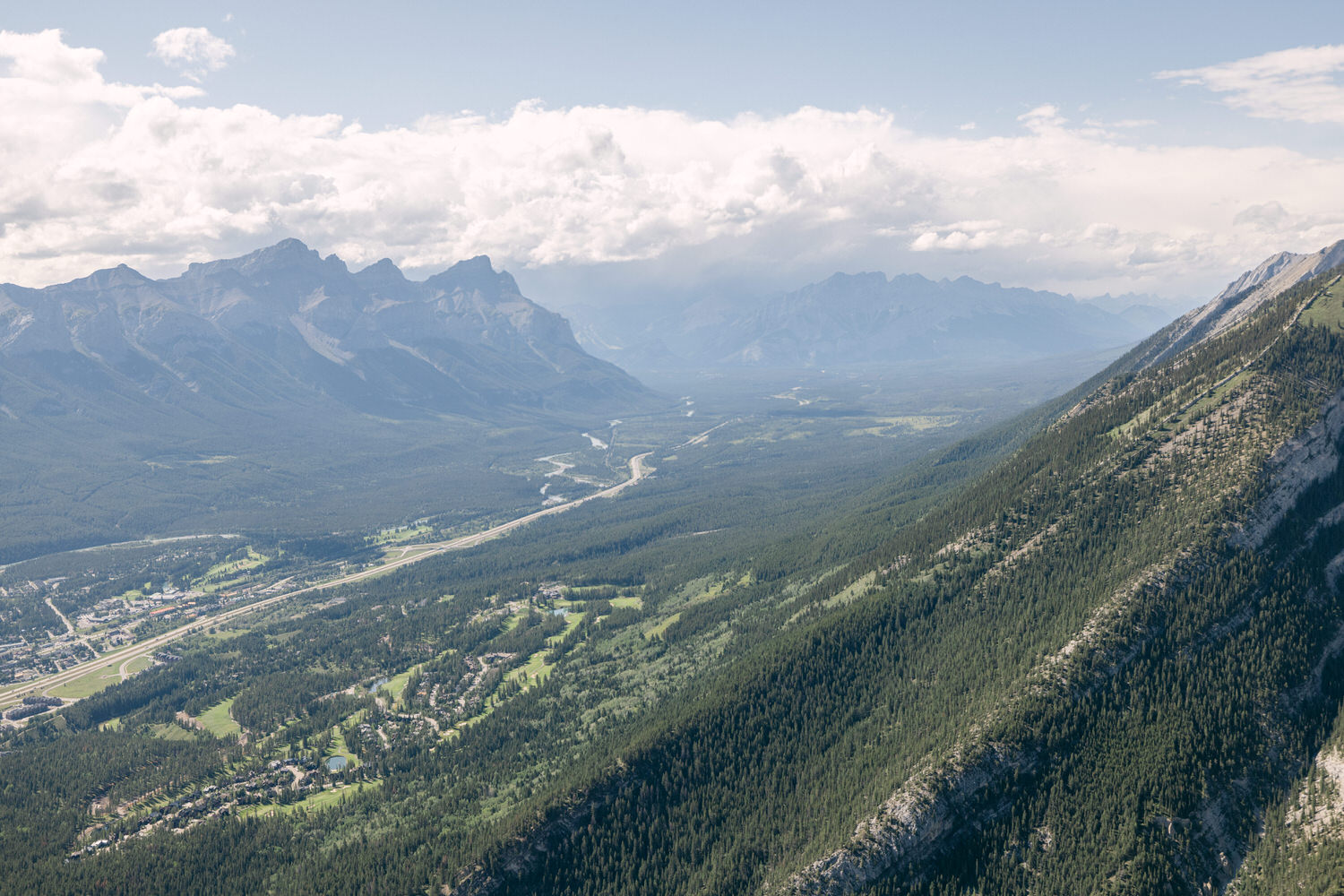 A panoramic view of a lush green valley surrounded by majestic mountains under a partly cloudy sky.