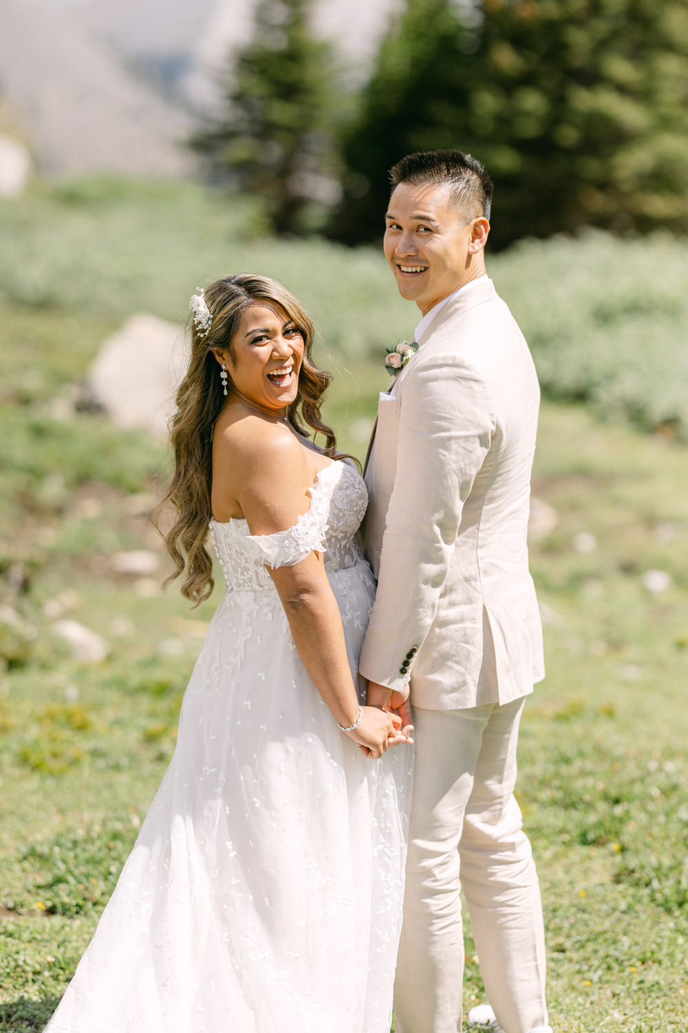 A happy couple holds hands and smiles at each other, surrounded by a beautiful outdoor setting.