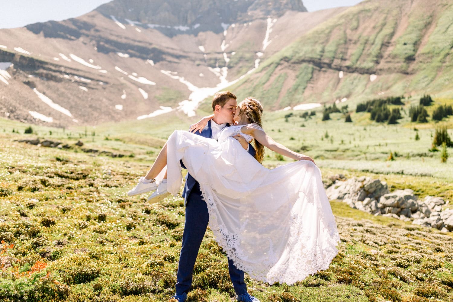 A couple kisses passionately as the groom lifts the bride in a picturesque mountain landscape.