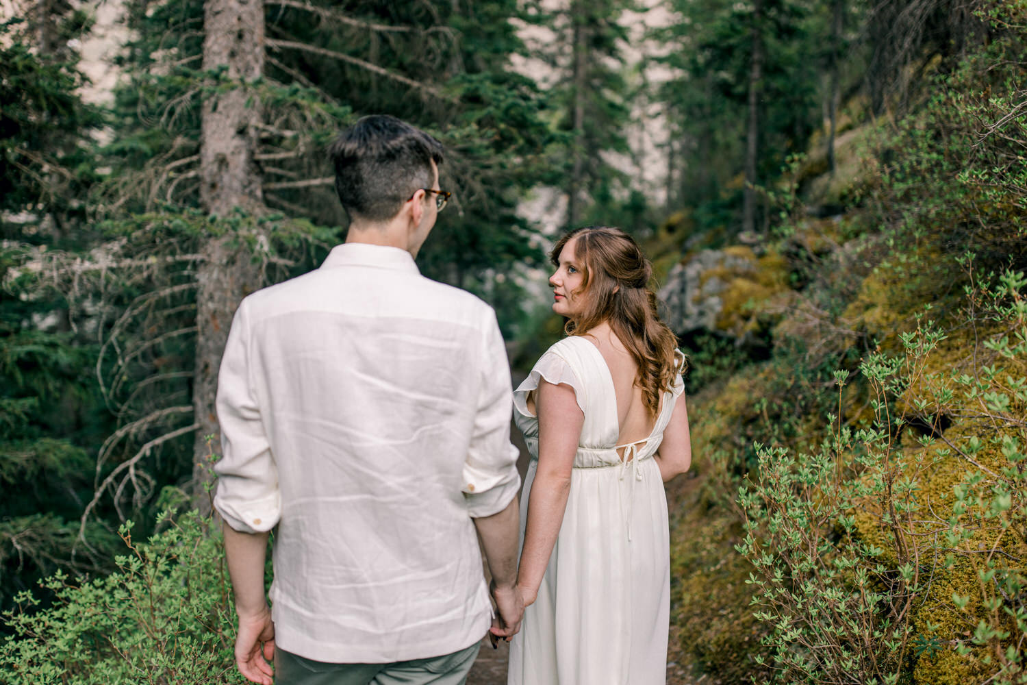 A couple walking hand in hand through a forest path, showcasing a serene moment surrounded by lush greenery.